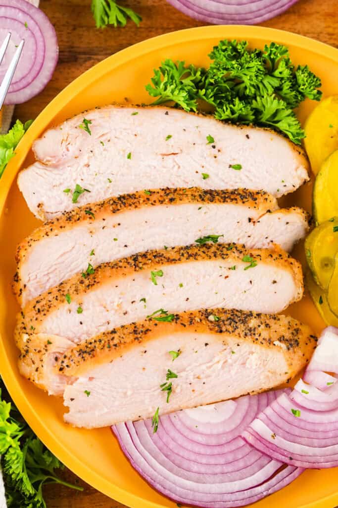 Overhead shot of peppered smoked turkey slices served with parsley, onions, and pickles