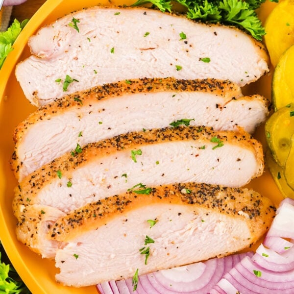 Square image of sliced smoked turkey breast with black pepper crust and fresh garnishes