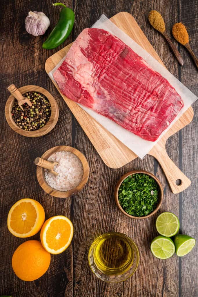Raw flank steak on a cutting board surrounded by fresh ingredients