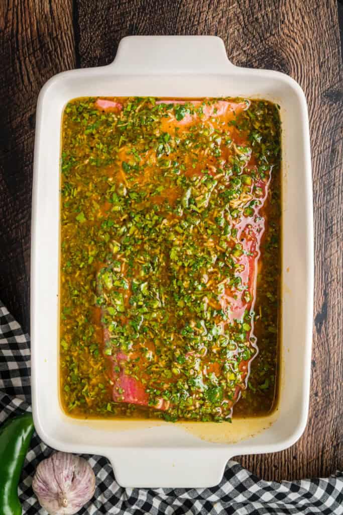 Flank steak marinating in a white baking dish with citrus herb marinade