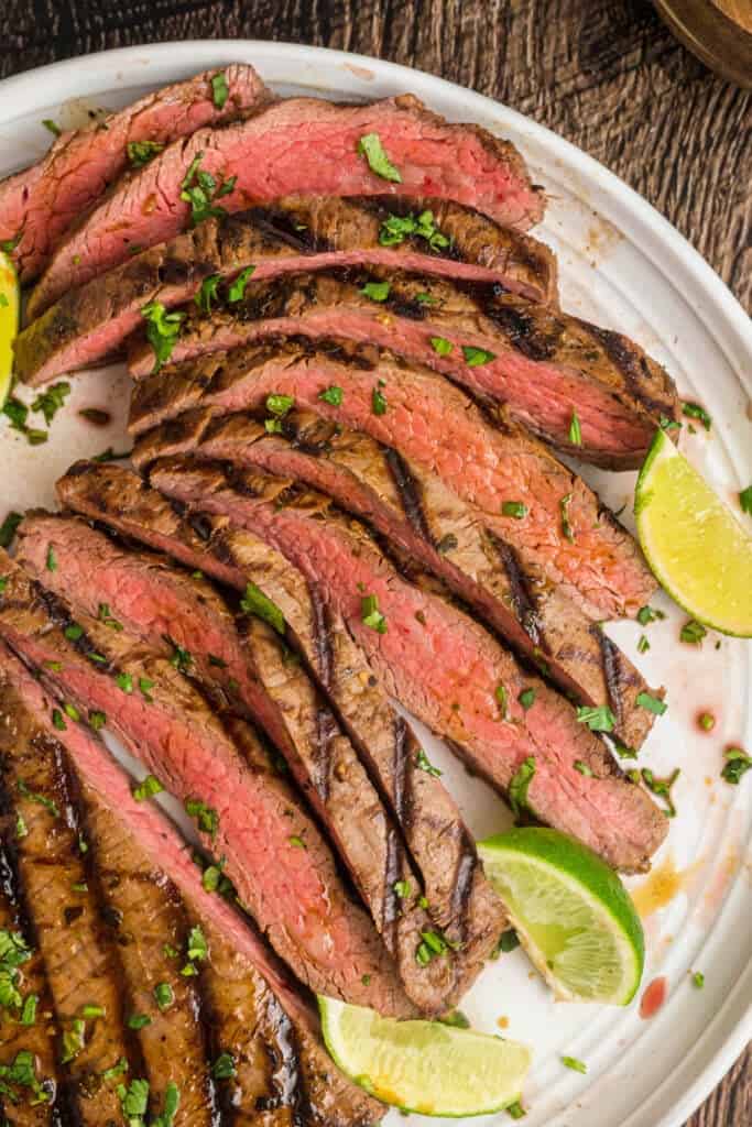 Sliced grilled carne asada steak on a plate garnished with lime wedges