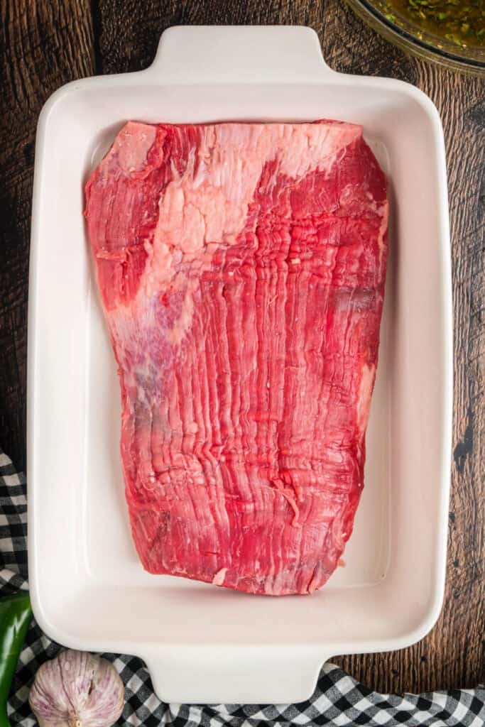 Raw flank steak placed in a white baking dish before marinating