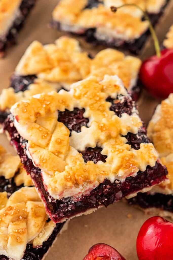 Close-up of a cherry pie bar with braided and crimped lattice topping, surrounded by cherries