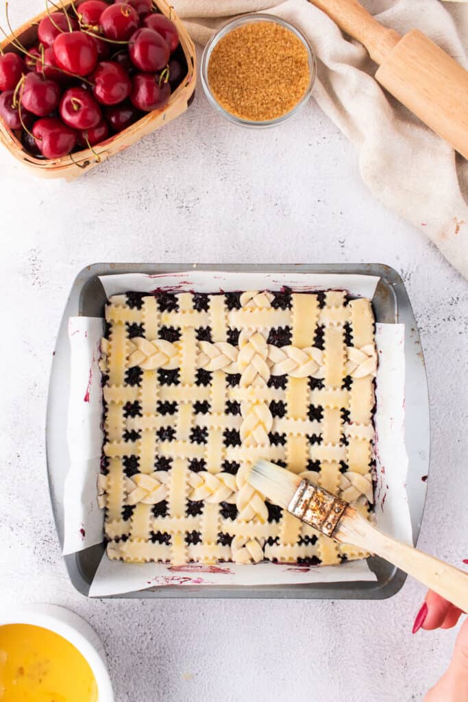 Unbaked cherry pie bars with lattice crust being brushed with egg wash