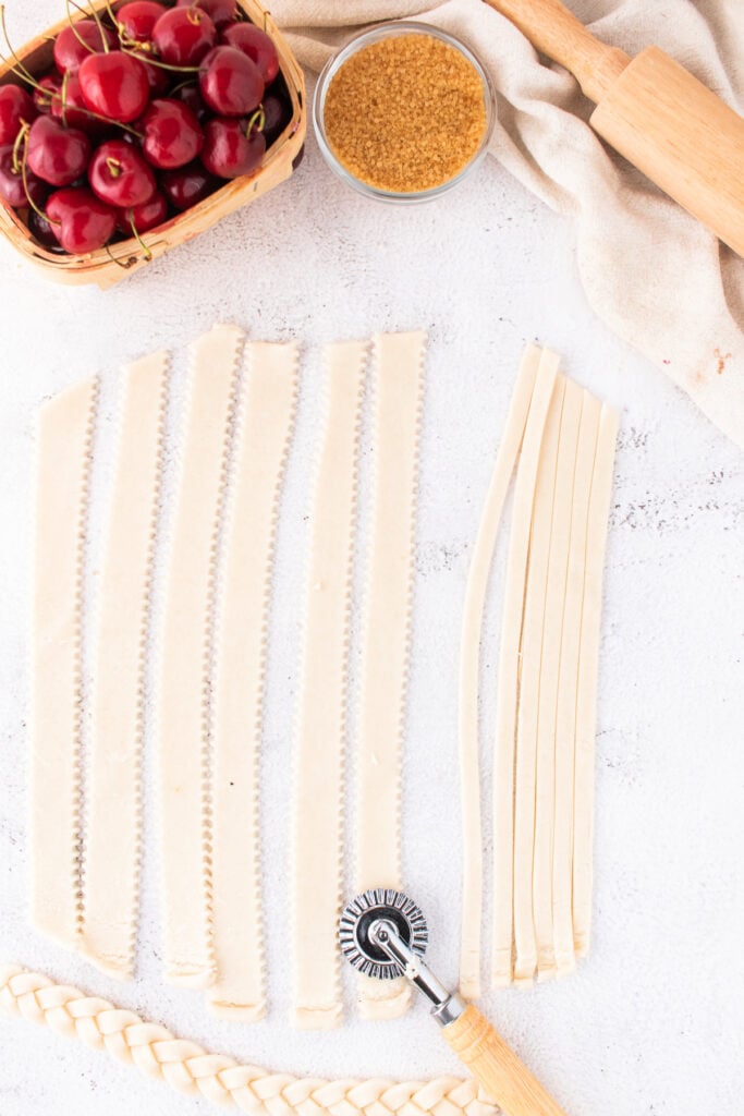 Strips of pie crust and braids ready for lattice assembly next to cherries and sugar