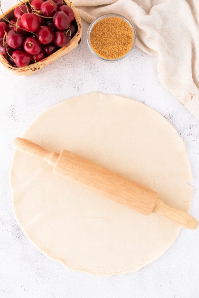 Rolled out pie crust with a wooden rolling pin on a white surface