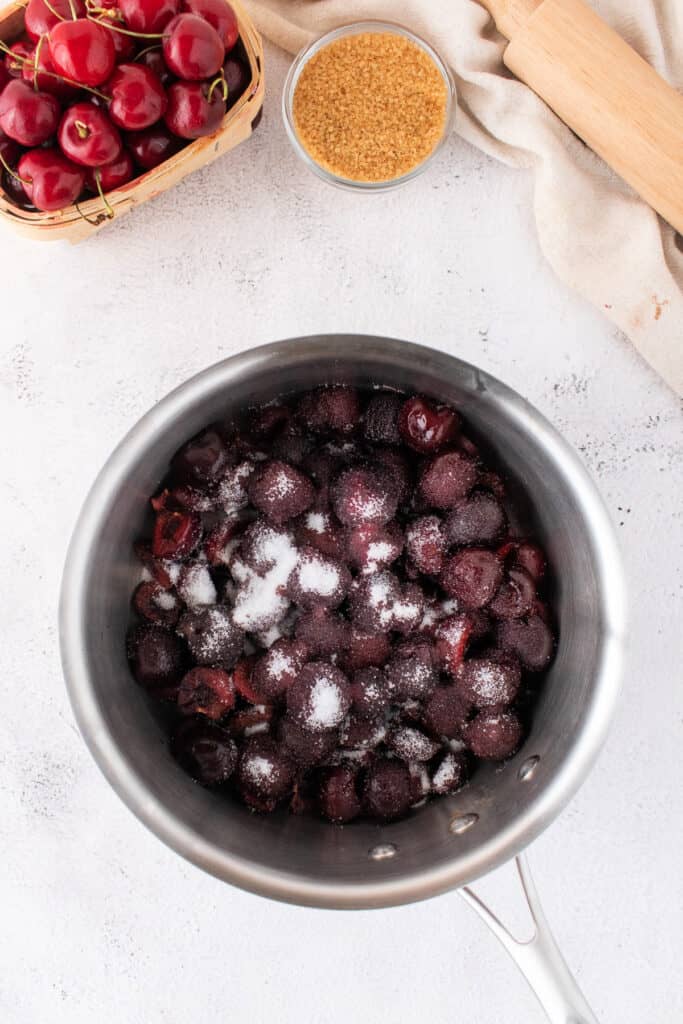 Frozen cherries sprinkled with granulated sugar inside a stainless steel saucepan