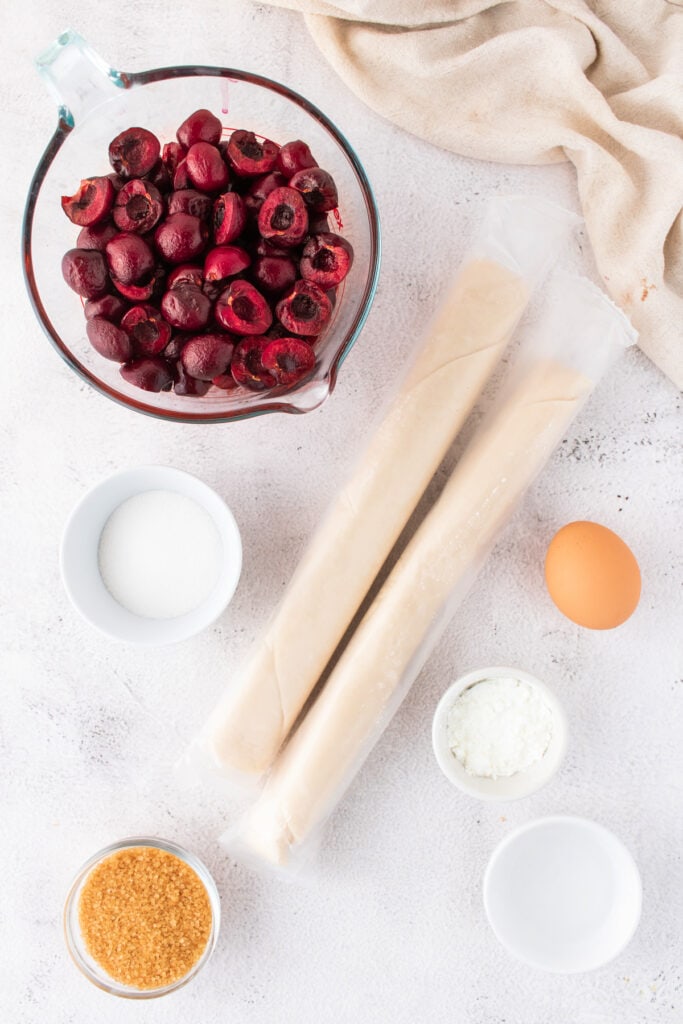Overhead shot of all cherry pie bar ingredients including cherries, pie crusts, egg, sugar, and cornstarch