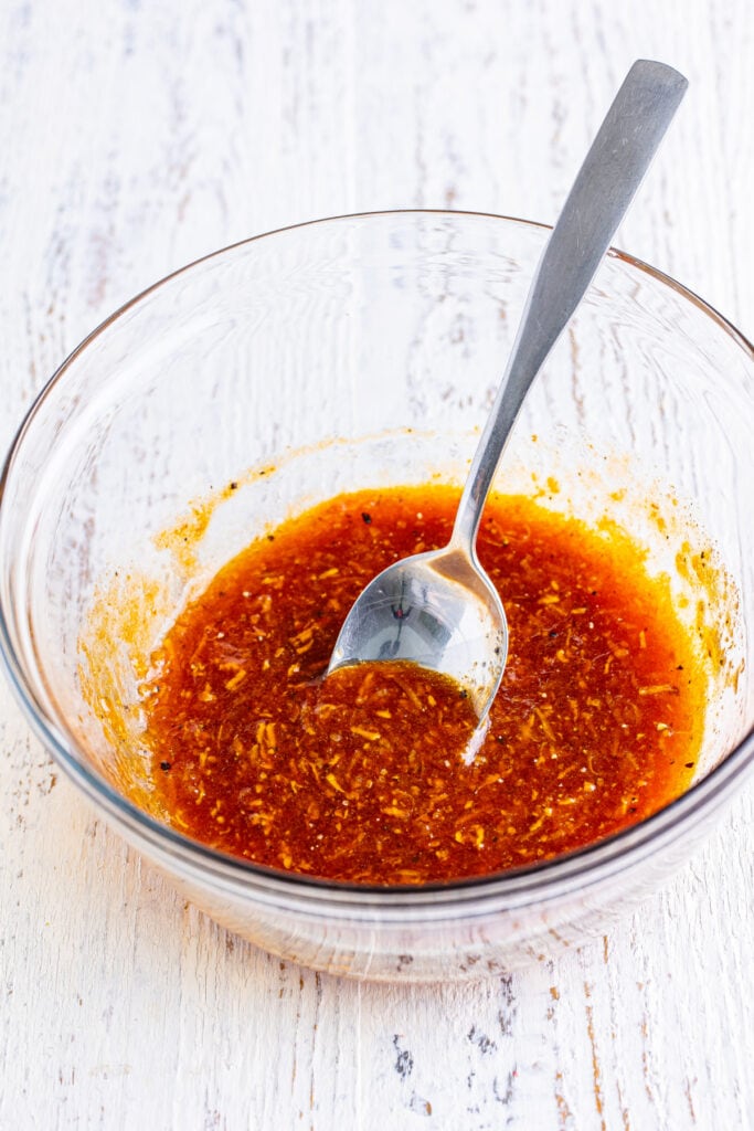 Mixed firecracker salmon marinade in a glass bowl with spoon.