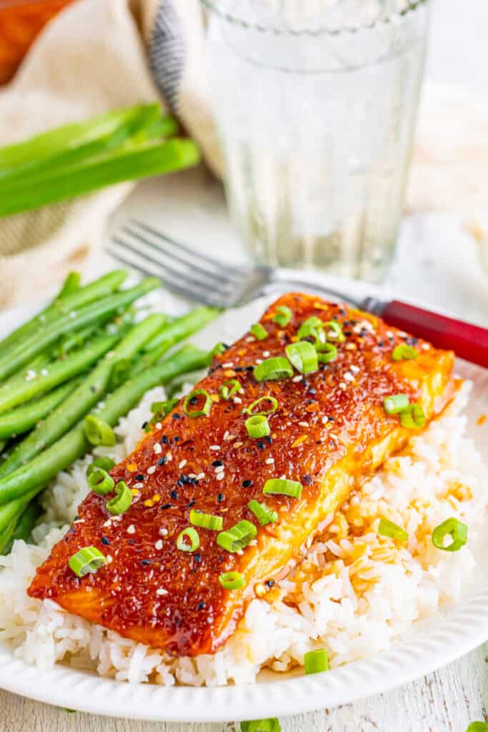 Plate of firecracker salmon over rice with green beans and a glass of water in background.