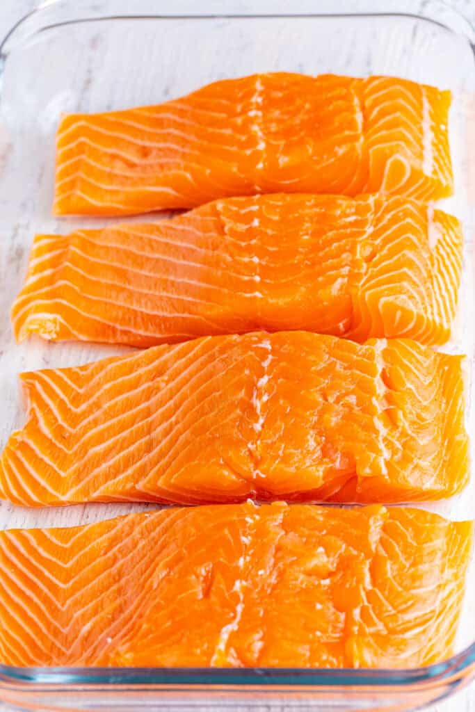 Raw salmon fillets lined up in a glass baking dish, ready for marinade.