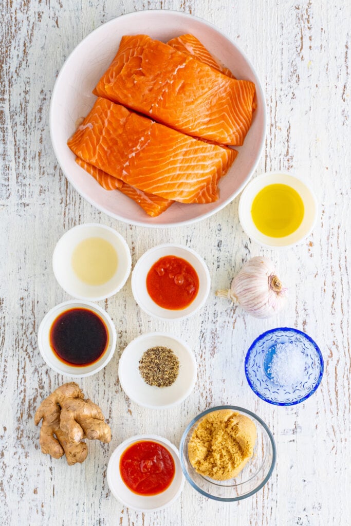 Flat lay of raw salmon and individual marinade ingredients in small bowls.