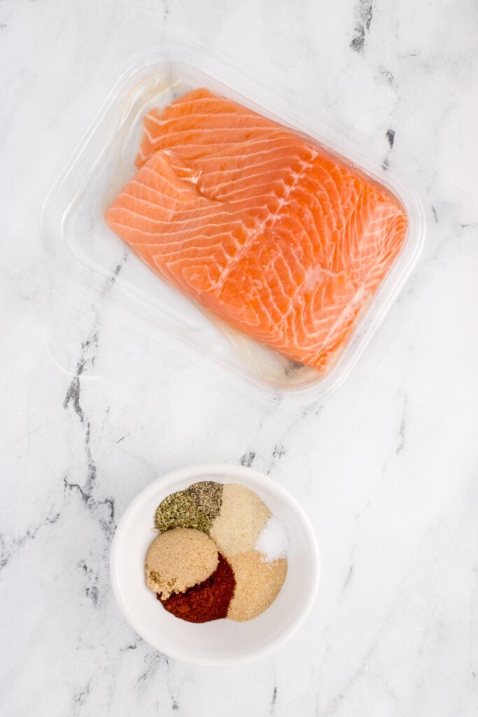 Fresh salmon fillets in packaging with a small bowl of blackened seasoning spices.
