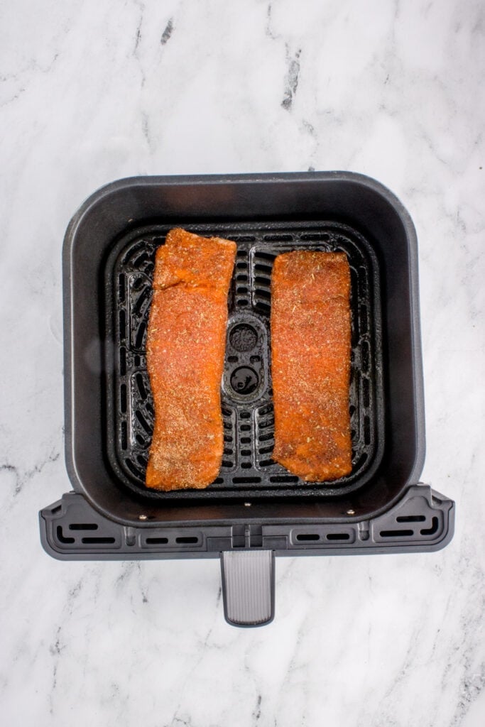 Salmon fillets placed in the air fryer basket before cooking.