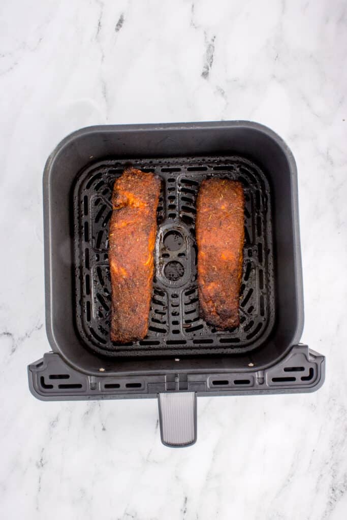 Cooked blackened salmon fillets in the air fryer basket after air frying.