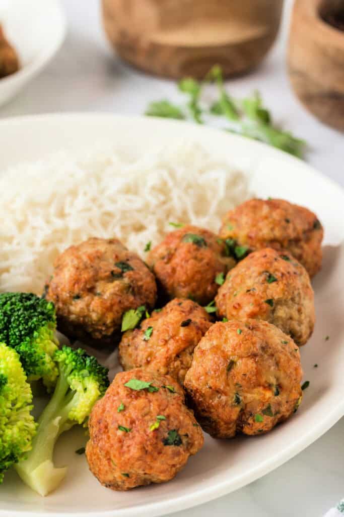 Plate of golden air fryer chicken meatballs served with broccoli and rice, garnished with fresh parsley