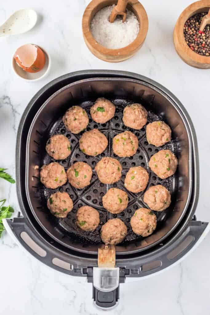 Uncooked chicken meatballs arranged in a single layer inside the basket of an air fryer before cooking