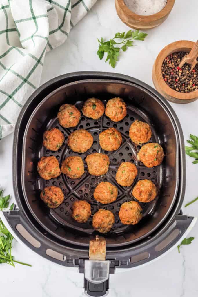 Golden brown chicken meatballs cooked in the air fryer basket with seasonings and herbs visible