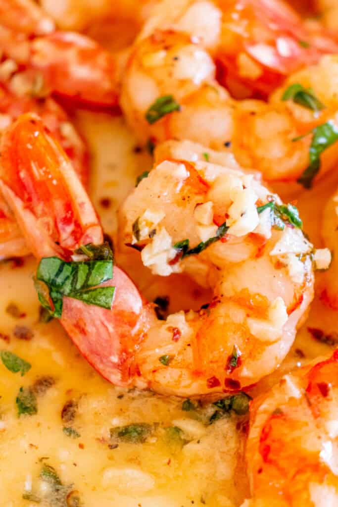 Extreme close-up of shrimp covered in garlic butter sauce, showing parsley and minced garlic pieces.