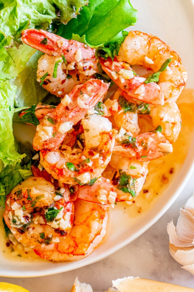 Plate of cooked shrimp tossed in garlic butter, garnished with parsley, served with lettuce on the side.