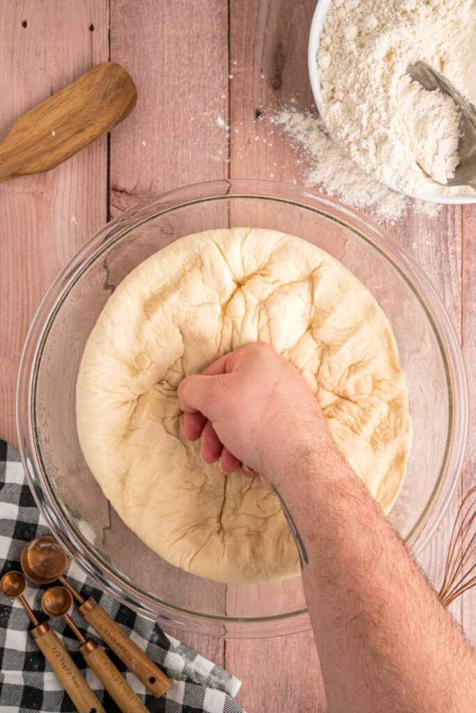 A hand punching down the risen dough to release air before shaping.