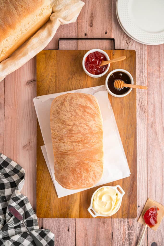 	Whole loaf of Amish white bread on a wooden board with bowls of jam, honey, and butter nearby
