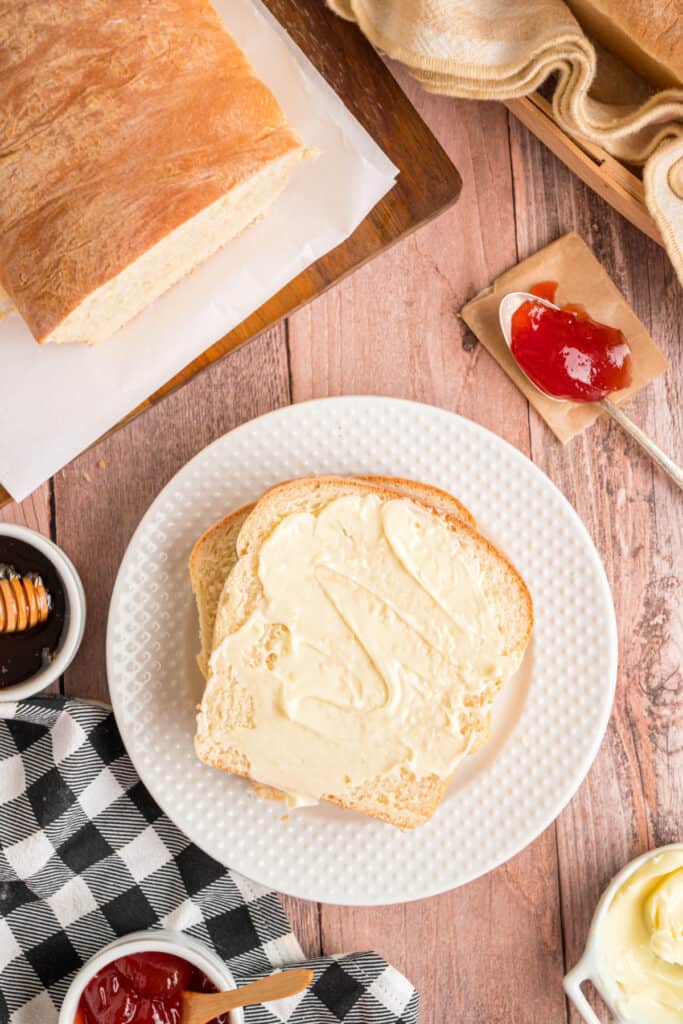 Two slices of Amish white bread on a plate with butter spread and jam on the side