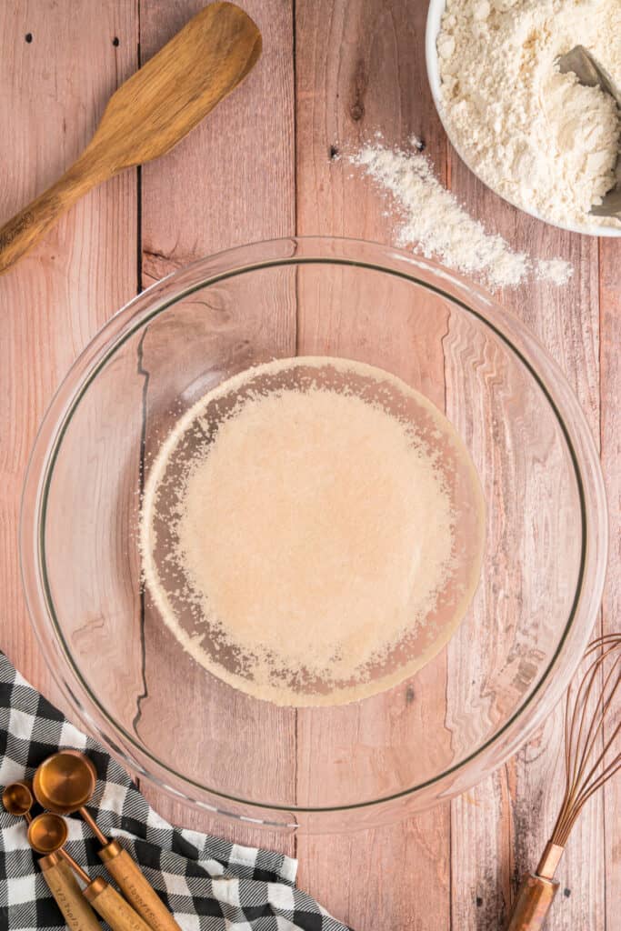 Yeast sitting on top of the sugar-water mixture in a glass bowl, beginning to activate.