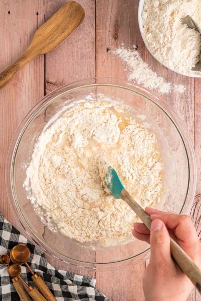 A hand mixing the ingredients with a spatula as the dough begins to come together.
