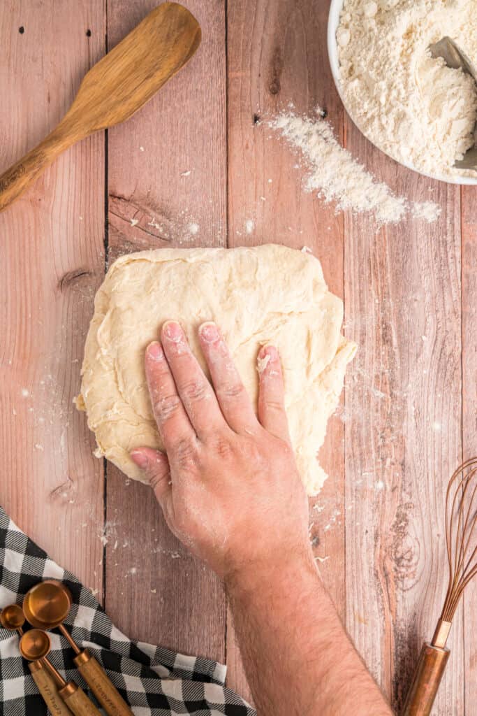 A hand kneading the dough on a floured surface during Amish white bread preparation.
