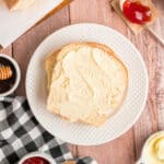 Square crop of two slices of Amish white bread with butter on a white plate, surrounded by jam and honey
