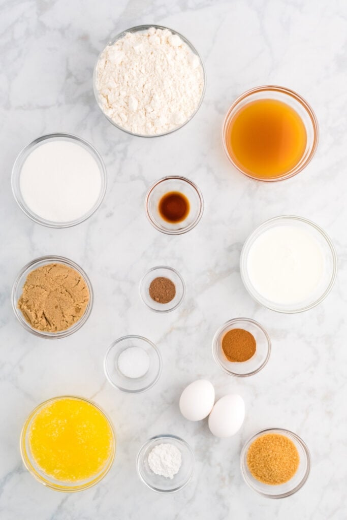 Overhead shot of measured ingredients in small glass bowls for apple cider muffins on a marble surface.