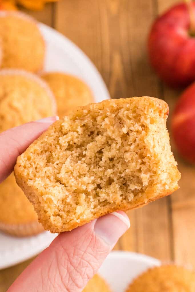 Hand holding a half-eaten apple cider muffin, showing the fluffy and moist interior crumb texture.