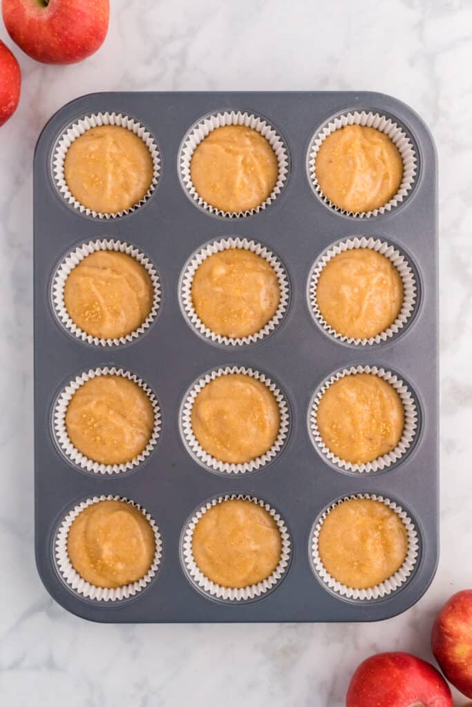 Muffin pan filled with apple cider muffin batter before baking, sprinkled with coarse sugar on top.