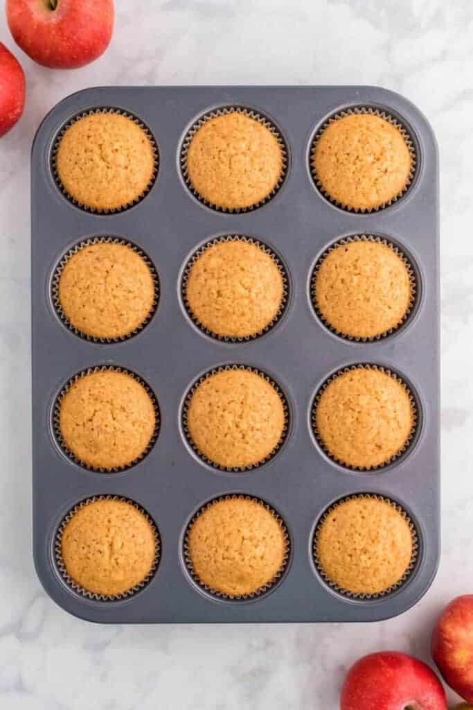 Freshly baked apple cider muffins still in the muffin pan, golden brown and fluffy.