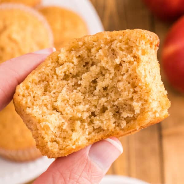 Square close-up of a hand holding a half apple cider muffin, highlighting the moist and fluffy inside texture.