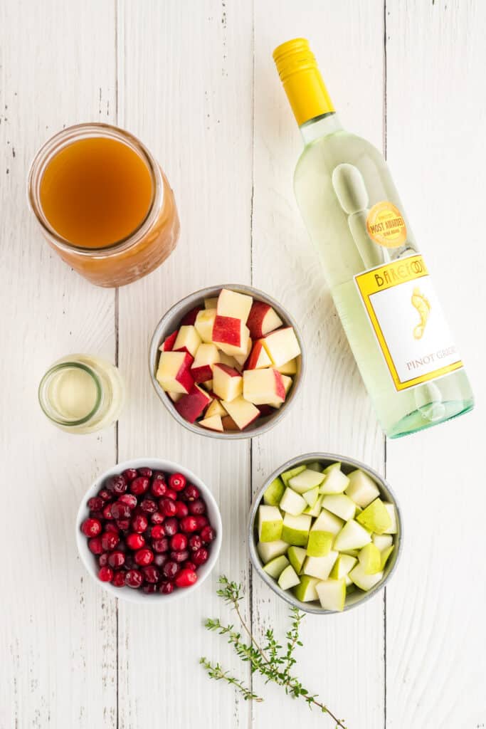 Overhead view of ingredients for apple cider sangria including apples, pears, cranberries, wine, and apple cider