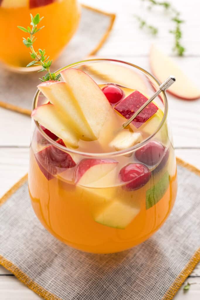 Side view of apple cider sangria in a stemless wine glass with fresh fruit and herbs