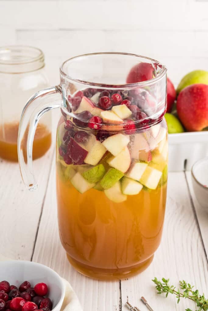 Pitcher filled with chopped fruit, apple cider, and white wine for making apple cider sangria