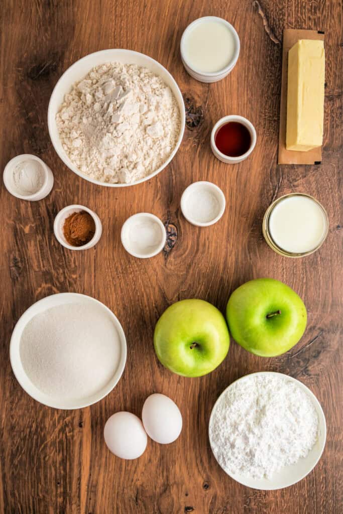Overhead shot of measured apple fritter bread ingredients, including flour, butter, sugar, eggs, apples, and spices on a wooden table.