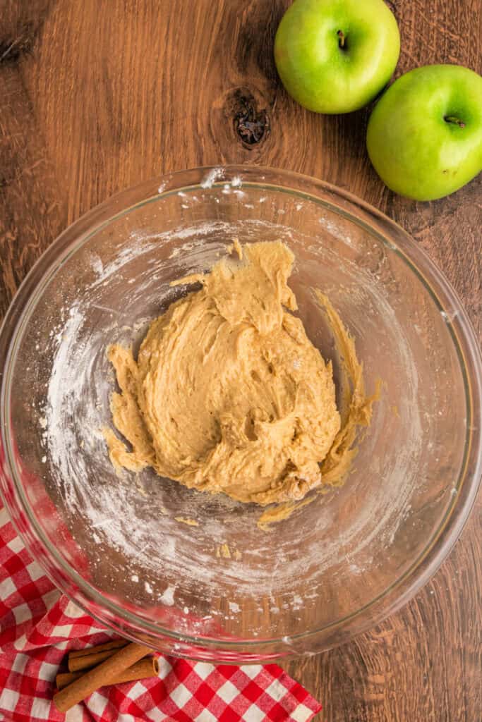 Apple fritter bread batter coming together in a large glass bowl after mixing flour into wet ingredients.