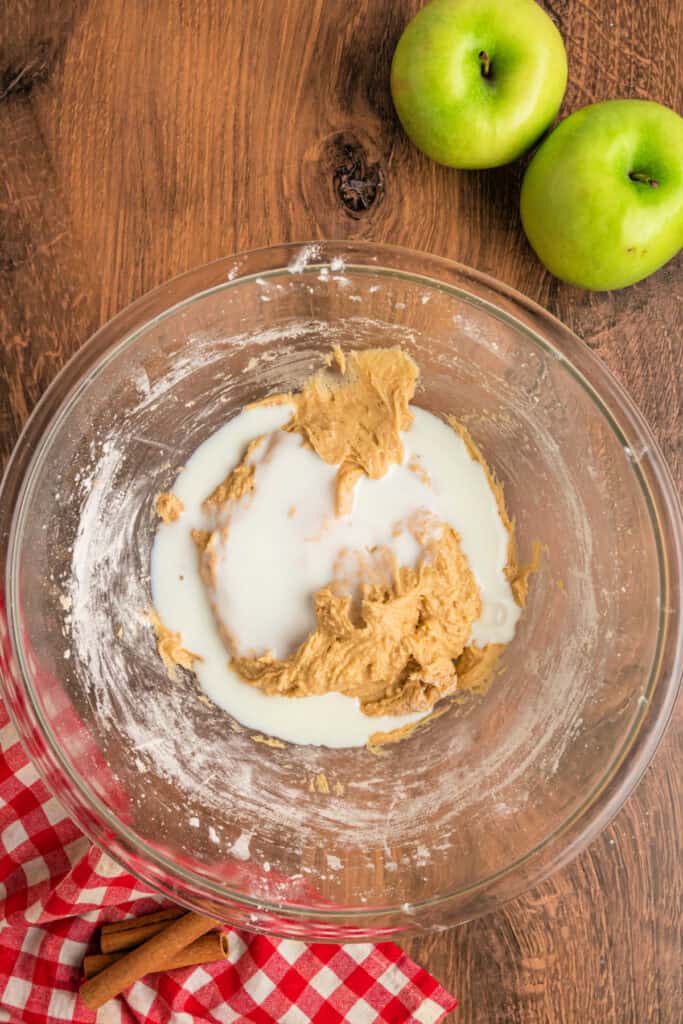 Glass mixing bowl with partially mixed apple fritter bread batter and milk on top, ready to be stirred.