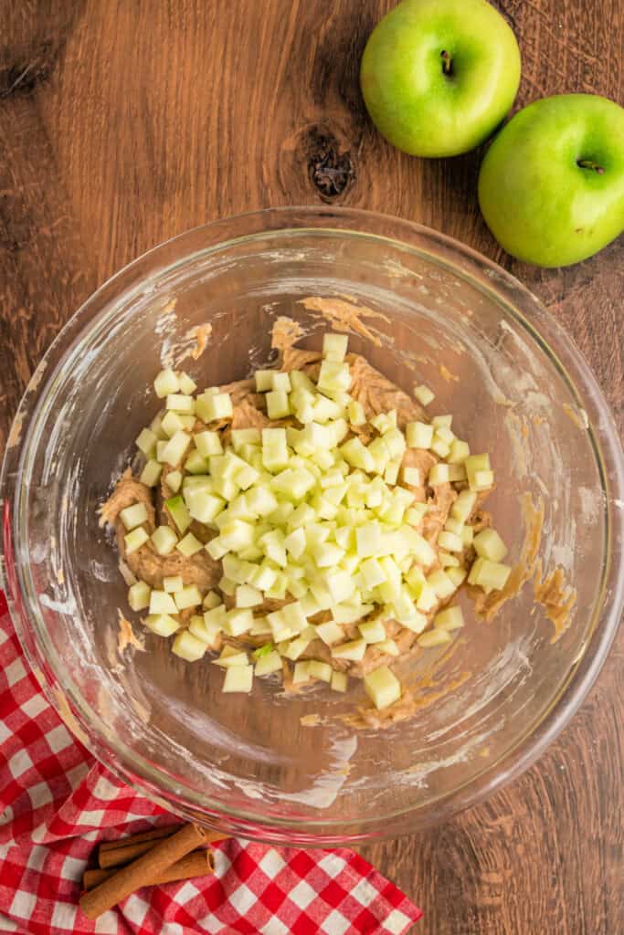 Glass bowl with apple fritter bread batter topped with freshly chopped green apple pieces.