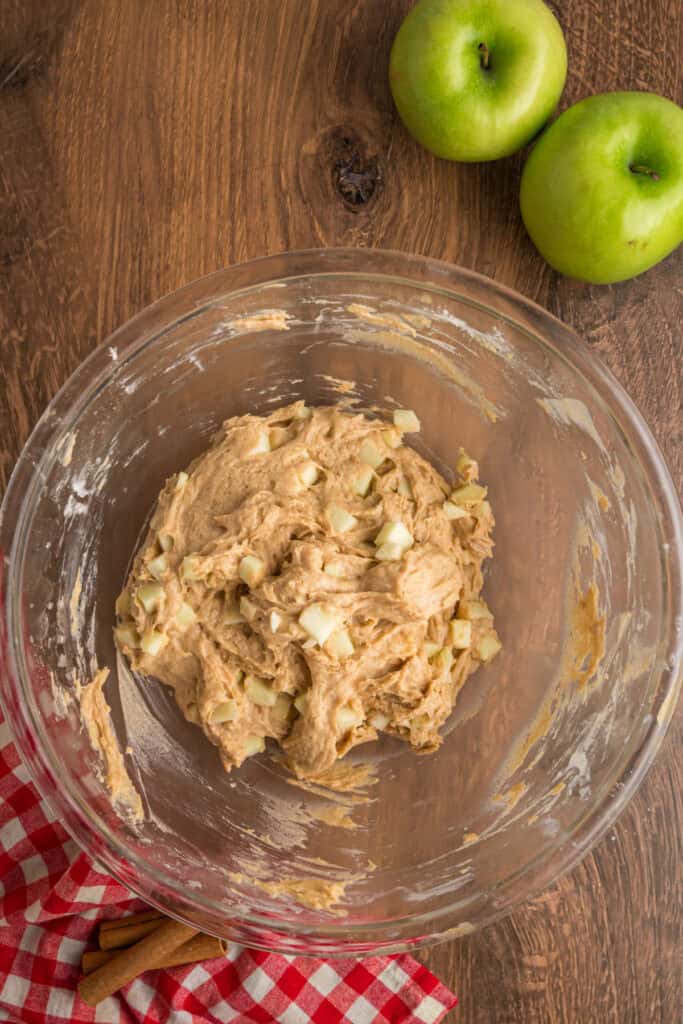 Thick apple fritter bread batter mixed with diced apples in a glass bowl, ready for the pan.