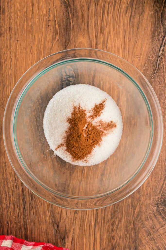 Bowl of granulated sugar with ground cinnamon sprinkled on top for the apple fritter bread filling.