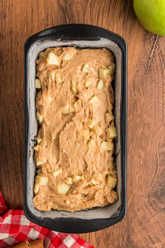 Loaf pan filled with apple fritter bread batter, showing chunks of apple throughout.