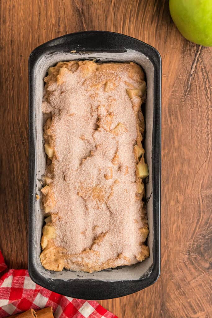 Loaf pan topped with an even layer of cinnamon-sugar mixture before baking apple fritter bread.