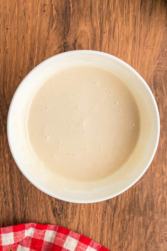Smooth vanilla glaze mixture in a white bowl, ready to drizzle over apple fritter bread.