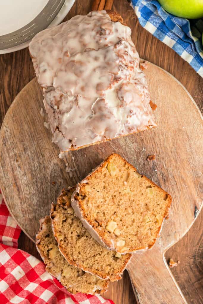 Glazed apple fritter bread sliced on a wooden board, showing tender apple-filled interior.