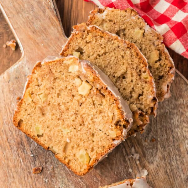 Overhead view of sliced apple fritter bread on a wooden board with a red checkered napkin, ready to serve.